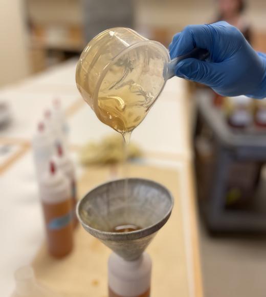 honey being poured from a glass dish through a funnel, into a plastic squeeze bottle