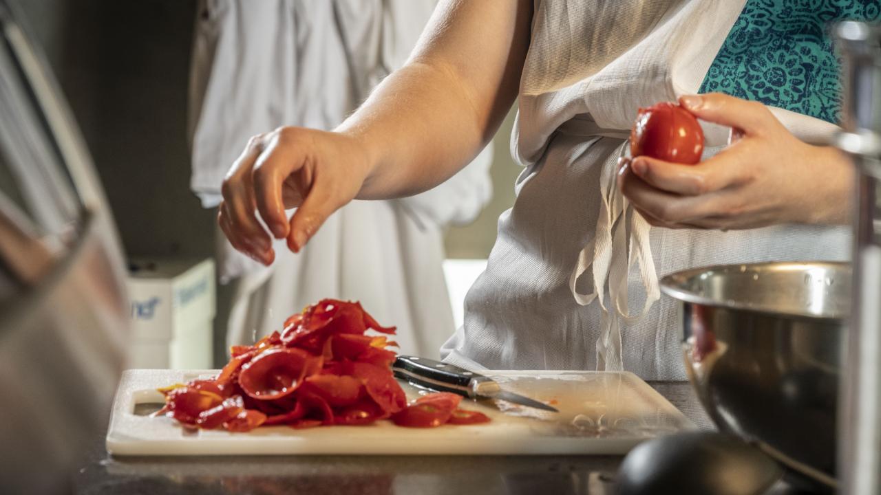 person in apron, peeling tomatoes with a knife and cutting board full of skins.