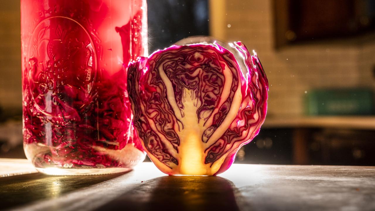 Glass jar of red brine and cabbage next to a cut half-head of red cabbage. 