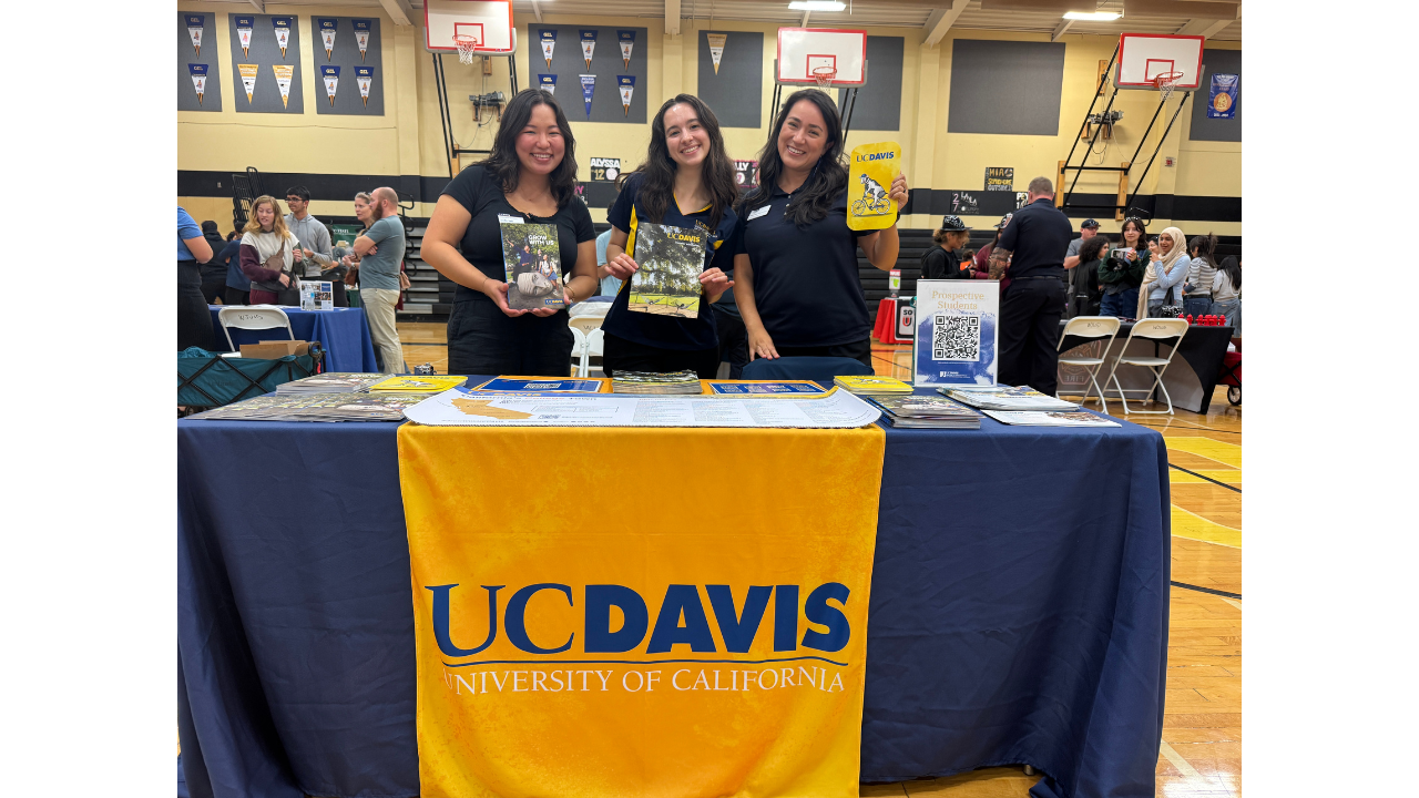 Three women posting at a table with materials at an outreach event.