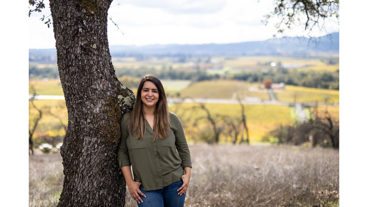 Priyanka Dhar French stands against a tree with a vineyard in the background