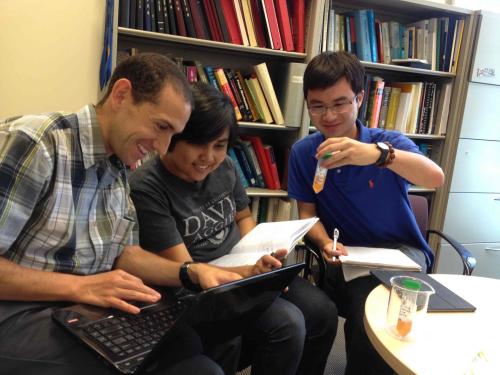 Researchers Tonio, Irna, and Kevin sitting at table together with laptop and a test tube