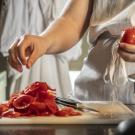 person in apron, peeling tomatoes with a knife and cutting board full of skins.