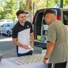 A seller and a prospective buyer meet over a table at the Davis Farmer's market. Product is on the table. 