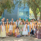 Large group of young adults in formal attire with gold stoles posing outdoors under trees