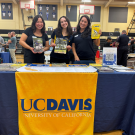 Three women posting at a table with materials at an outreach event.