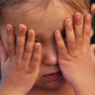 A kid putting her hands on her eyes